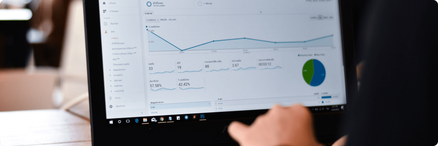 Close-up of a person using a laptop displaying analytics software, vital for any digital marketing agency. The screen shows a line graph, pie chart, and various statistics. The users hand is partially visible on the keyboard, with a blurred background of an indoor setting.