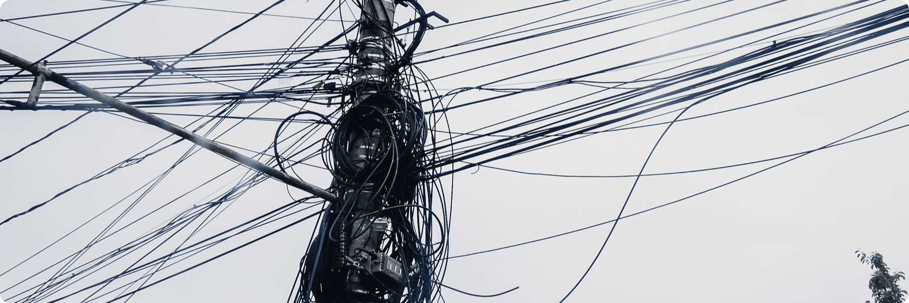 A utility pole with numerous tangled electrical wires against a light gray sky resembles the intricate strategies of a digital marketing agency, where cables symbolize the complex and chaotic network of SEO services extending in multiple directions.