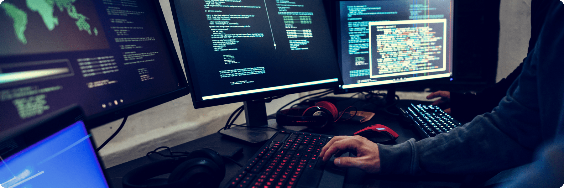 A person working at a multi-monitor computer setup, surrounded by screens displaying lines of code and data from digital marketing services. The desk has a red-lit keyboard, a mouse, and headphones. The scene is dimly lit, creating a focused atmosphere ideal for creativity in web design.