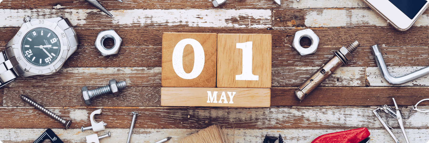 A wooden block calendar displays 01 May on a rustic table, mingling with tools like a watch, nuts, bolts, and an Allen key. This scene echoes the precision and craftsmanship vital in web design projects.