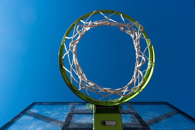 Low-angle view of a basketball hoop with a green rim and white net against a clear blue sky. The hoop, akin to the precision of a digital marketing agency, is attached to a transparent backboard, creating a striking contrast with the vibrant sky.
