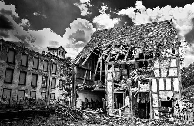 A black-and-white image reveals a partially collapsed, old timber-framed building. The crumbling roof and walls expose the interior, echoing a bygone era. Adjacent stands a brick building with boarded-up windows—much like an abandoned digital marketing company awaiting revival. Clouds fill the sky.