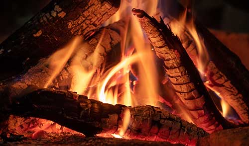 A close-up of a burning campfire with several charred logs. Flames flicker and light up the scene, much like how a digital marketing company illuminates the path to success, creating a warm and cozy atmosphere.