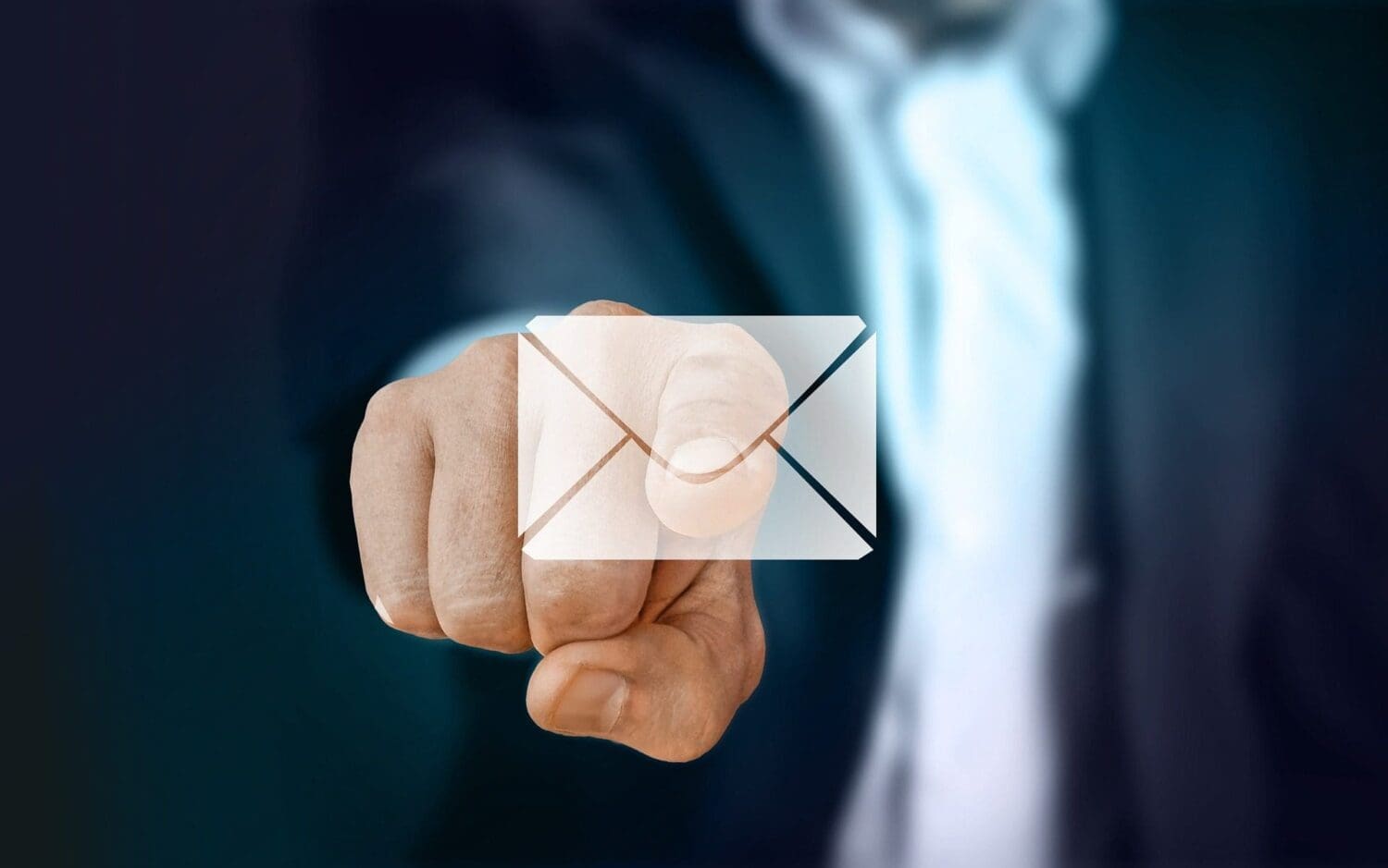 A person in a suit extends their hand, pointing forward. A digital overlay of an envelope icon appears on their finger, symbolizing email or digital communication—essential tools for any marketing agency. The background is blurred and dark.