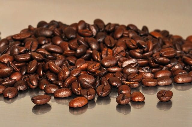 A close-up of roasted coffee beans scattered on a smooth, reflective surface, reminiscent of a sleek web design. The beans have a rich, glossy finish, showcasing various shades of brown.