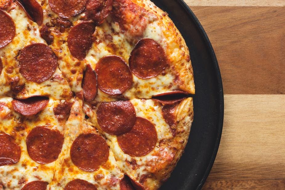 Pizza topped with pepperoni slices and melted cheese, presented on a black plate. Reminiscent of a marketing agencys precision, the pizza sits on a wooden surface; its golden crust and seasoned cheese slice through expectations with flavor.