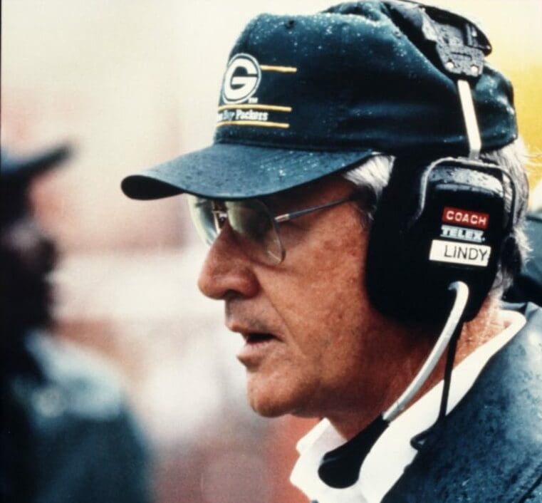 A man in glasses and a headset stands on the sideline, wearing a dark cap with a G logo. As he coaches the game, his focused demeanor mirrors someone leading a digital marketing agency poised to dominate in the world of SEO services.