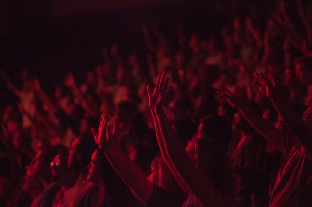 A crowd of people with their hands raised, bathed in red lighting, creates a vibrant and energetic atmosphere at what appears to be a concert or event hosted by a leading digital marketing agency.