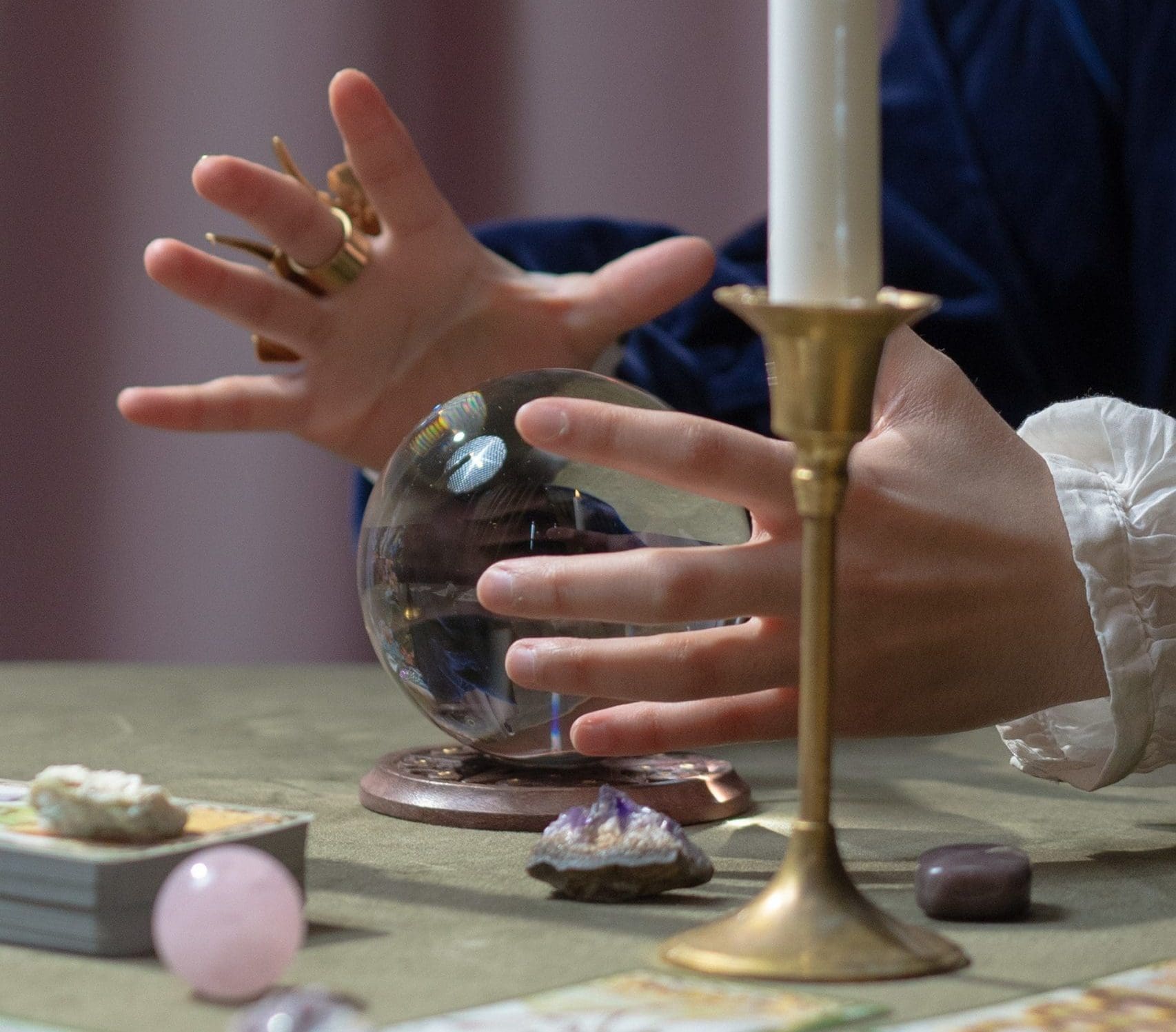 A person with decorative rings hovers hands over a crystal ball, surrounded by tarot cards, crystals, and a lit candle on a green tablecloth. The scene unfolds like the creative magic of a digital marketing agency crafting enchanting campaigns in a world of mystery.