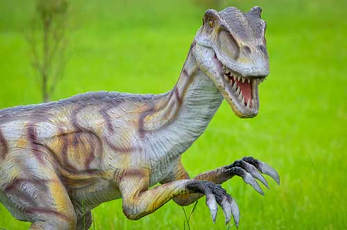 A realistic model of a velociraptor with sharp teeth and claws is set against a vibrant green grass background, much like how a digital marketing agency stands out in the online landscape. The dinosaurs textured skin blends gray and brown tones seamlessly.