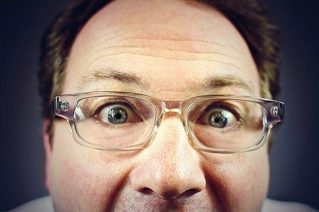 Close-up of a person wearing glasses, looking directly at the camera with a slightly surprised expression, as if theyve just discovered top-notch SEO services. The background is a plain, dark color.