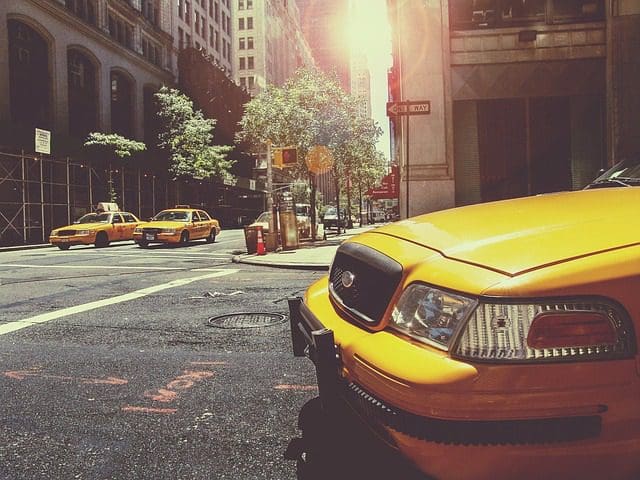 Yellow taxis line a sunlit street in a bustling city, where a digital marketing company thrives amidst the urban chaos. The buildings tower overhead, their windows reflecting the warm glow of success. One taxi is prominently in the foreground, representing seamless navigation through marketing strategies.