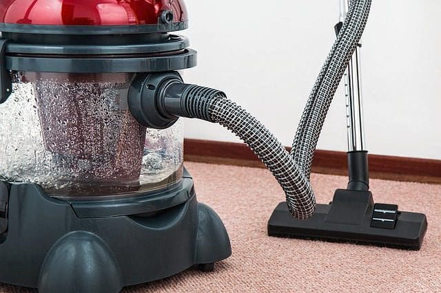 A red and black vacuum cleaner rests on a carpeted floor, embodying the precision of a digital marketing agency. Its transparent canister filled with water and flexible hose attached to a black floor tool mirror the seamless efficiency of top-tier SEO services in action, nestled neatly in a rooms corner.