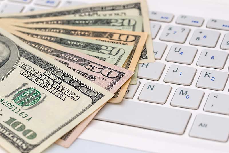 Several US dollar bills of various denominations are spread out on top of a white computer keyboard.